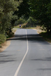 Cyclist riding through a lush rural trail surrounded by green trees and a glimpse of a waterfall in the background