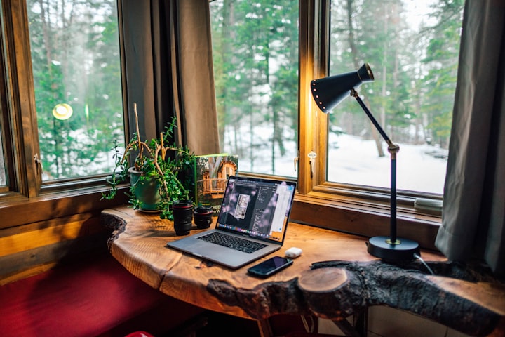 at home office a log table with a laptop on plant on it with a view of a snowy landscape out the window. 