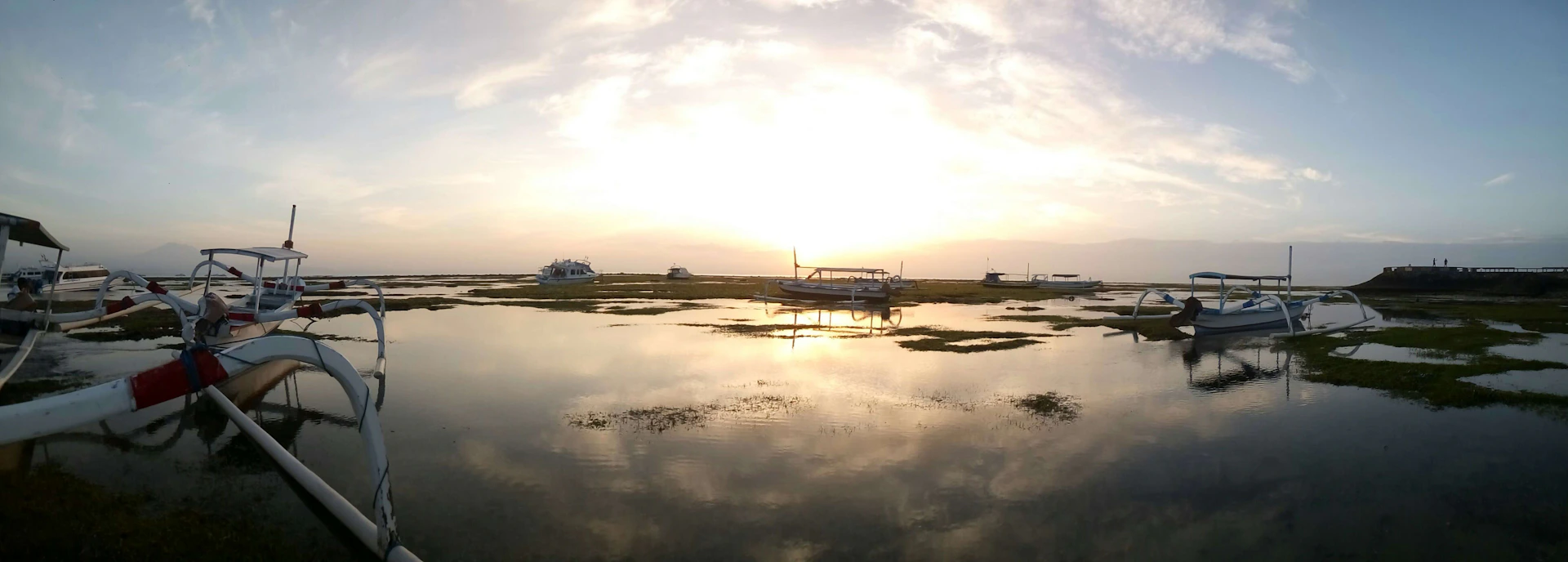 A peaceful riverside at sunset in West Africa, with traditional boats and warm golden light reflecting on the water.