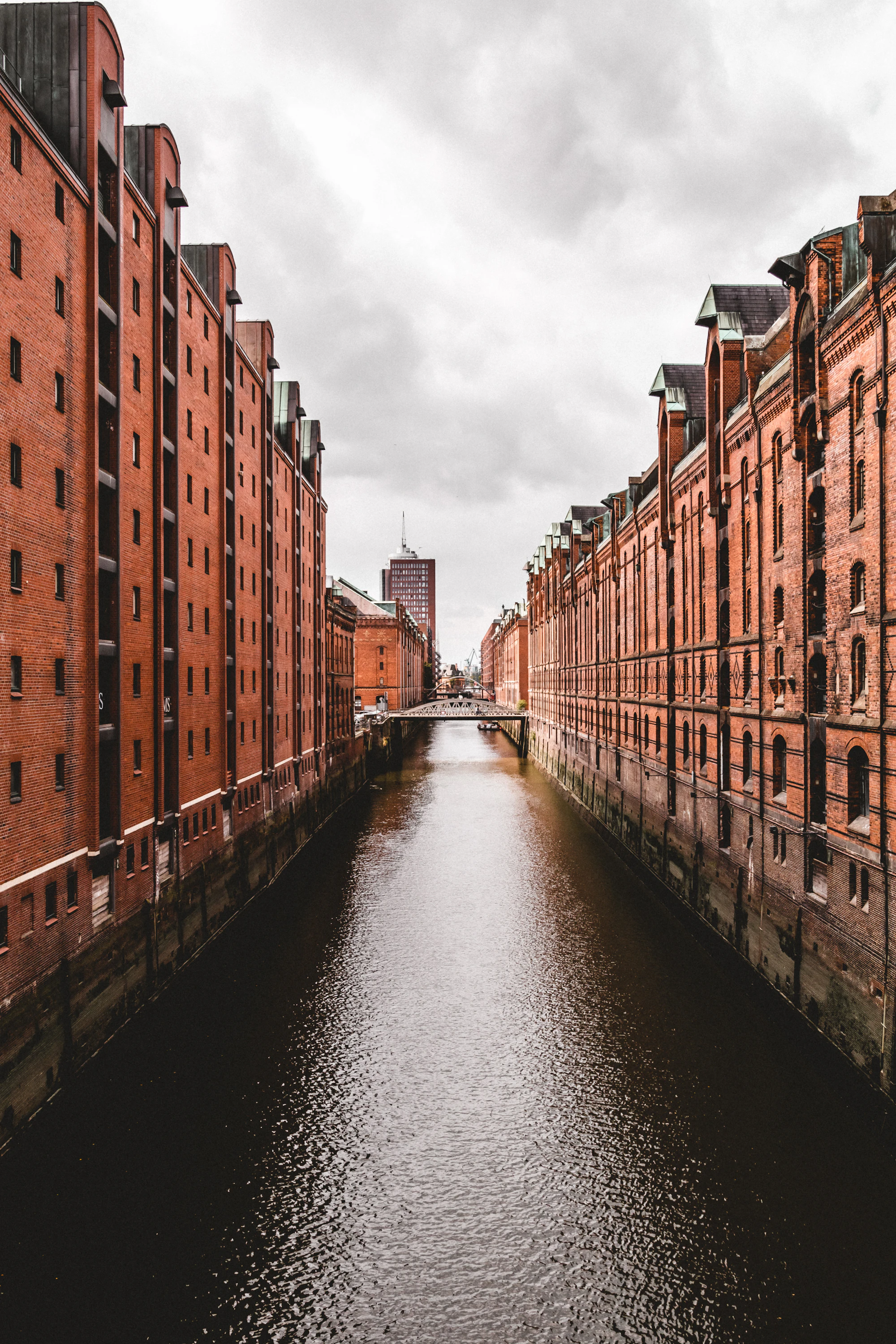 Warehouse buildings lining a narrow canal, both banks converging toward a distant bridge