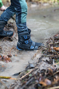 Wet leaves clinging to olive-green anti-leech socks as a boot moves through dense jungle undergrowth.