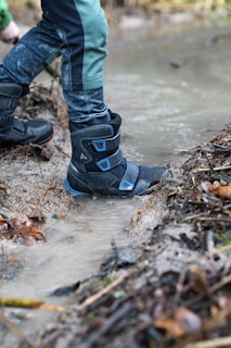 Close-up of boots splashing through a shallow stream during a hiking trail.