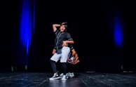 An adolescent performer mid-dance under a cool blue stage light, expression intense.