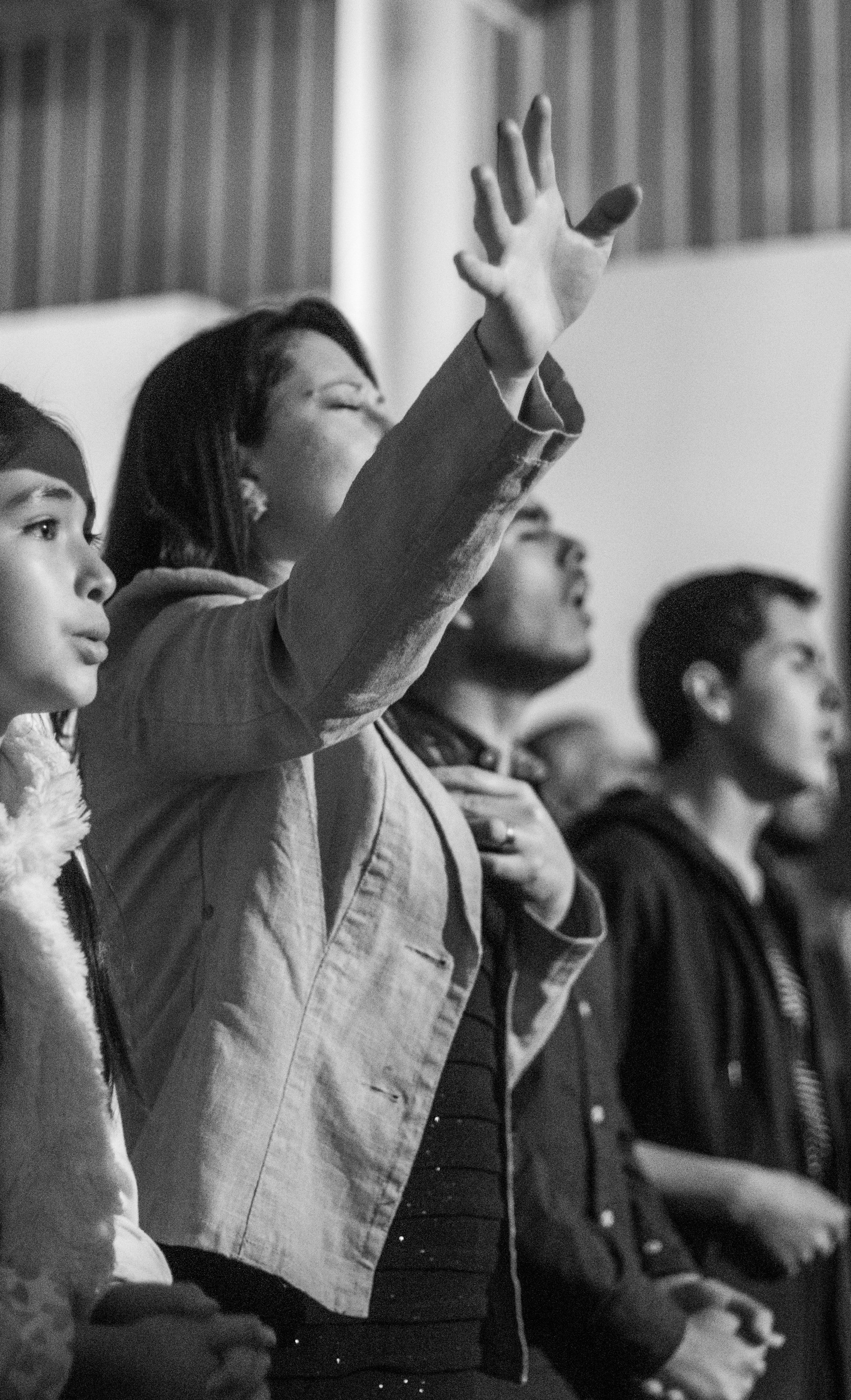People in church sanctuary with hands raised in worship, warm stage lighting, dimly lit atmospheric interior