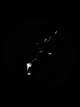 A dark background with a small flame or light source, creating a contrast against the black surroundings.
