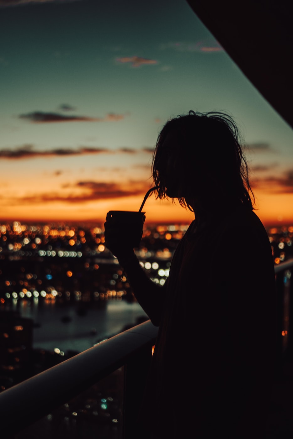 Mensch trinkt Mate Tee vor einer abendlichen Skyline