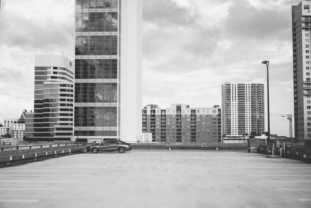 grayscale photography of vehicle parking with high-rise building background