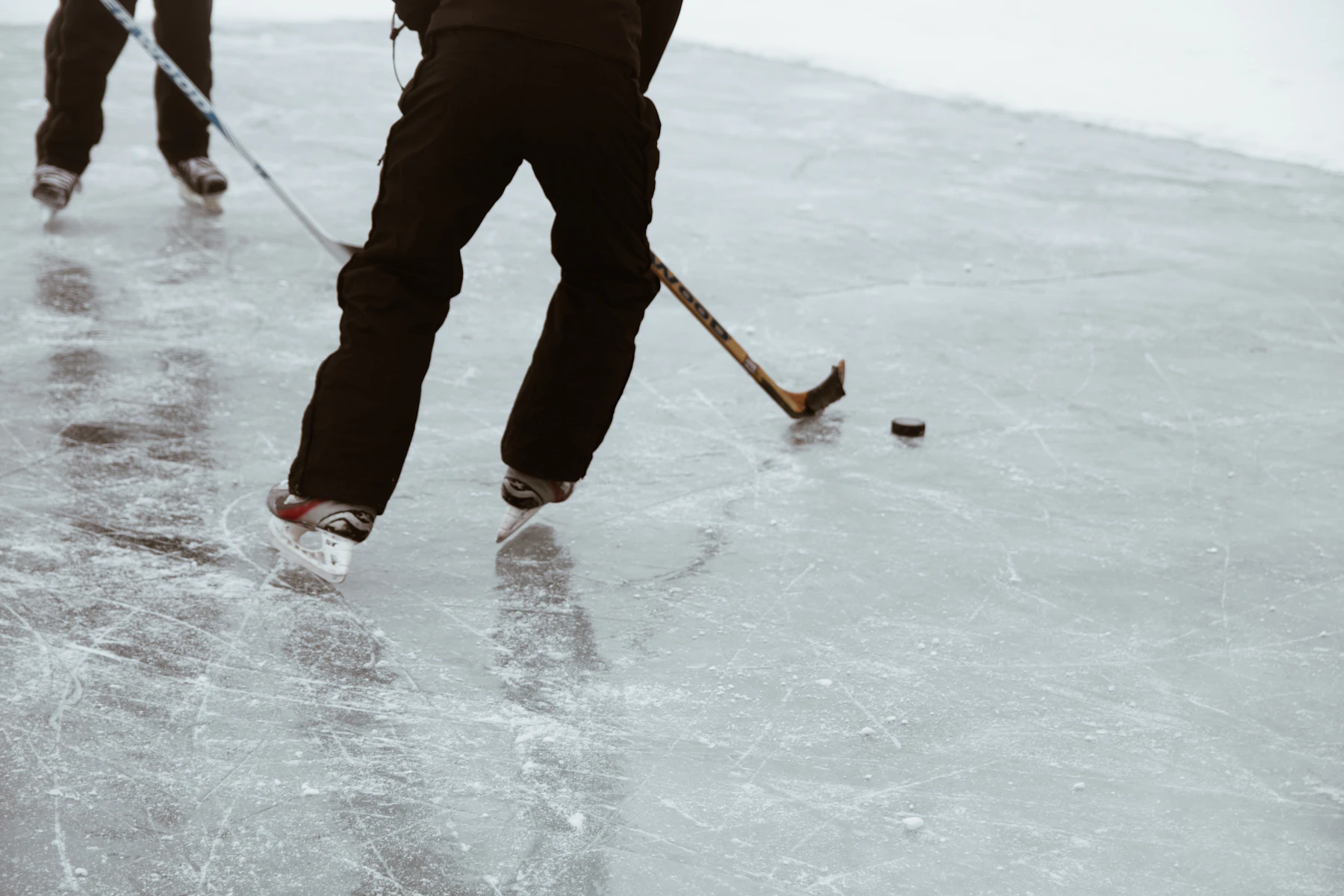 Close on a pair of skates, a hockey stick and a puck on scuffed gray outdoor ice