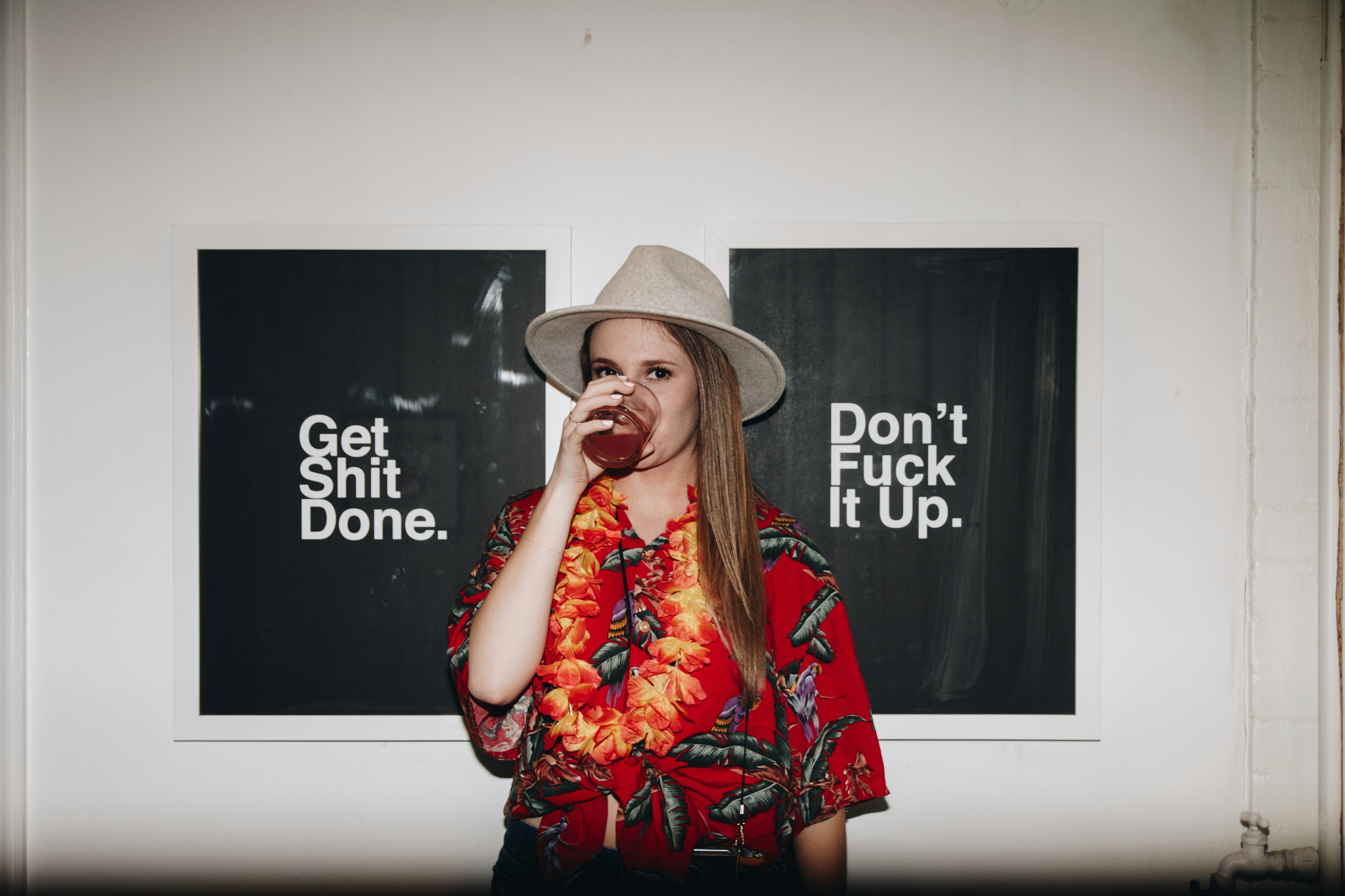 Mujer con camisa roja y sombrero gris bebiendo de un vaso