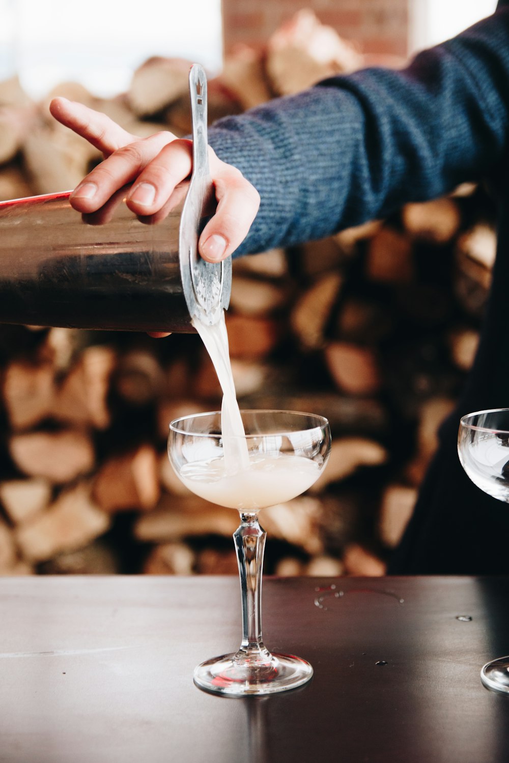 person pouring cocktail in footed glass