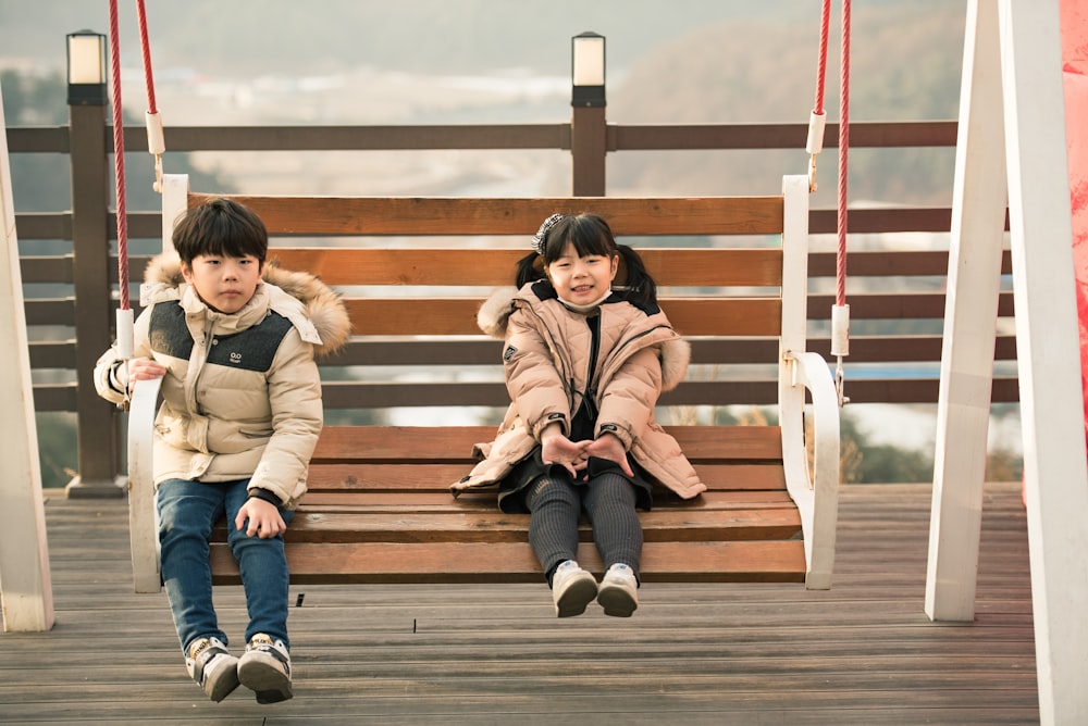 two children sitting at hanging bench