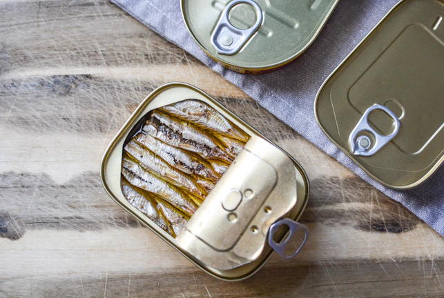 Close-up of a rustic table with an open can of sardines glistening in olive oil.