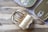 Three rectangular tin cans with pull tab openers, two of which are closed and one opened, reveal neatly packed fish (likely sardines). These tin cans are placed on a wooden surface partially covered by a grey cloth, providing a rustic setting.