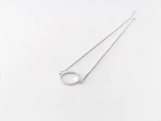 Close-up of a delicate silver necklace with a small pendant resting on a soft fabric background