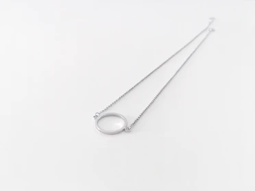 Close-up of a delicate silver necklace with a small pendant resting on a soft fabric background