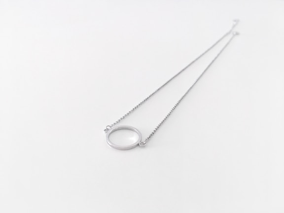 Close-up of a delicate silver necklace with a small pendant on a wooden surface.