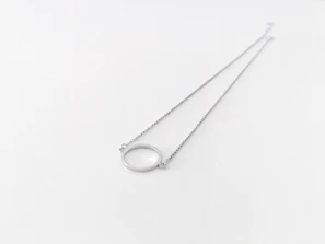 Close-up of a delicate silver necklace with a twin pendant resting on a marble surface.