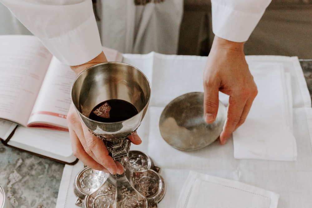 person holds chalice with liquid on table