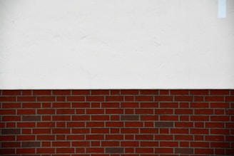 A simple composition featuring a horizontal division between a brick wall and a white plastered surface above.