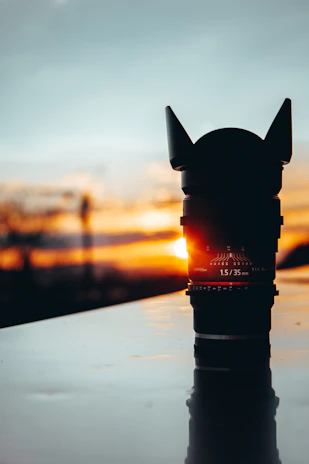 A minimalist, dark-themed photo of a camera lens reflecting a dramatic sunset over wild terrain.