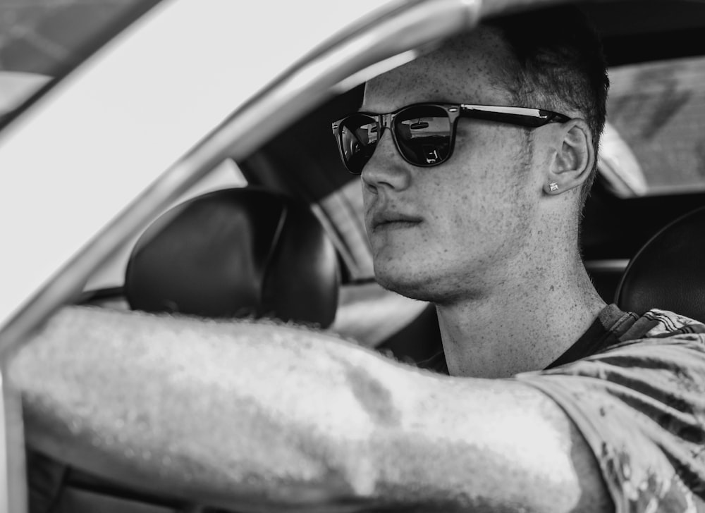 grayscale photo of man wearing sunglasses driving car