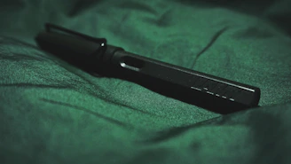 Close-up of a deep carmine red pen resting on matte forest green textured paper.