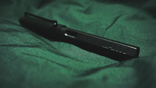 Close-up of a deep carmine red pen resting on matte forest green textured paper.