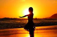 A silhouette of a person meditating at sunset on a beach.
