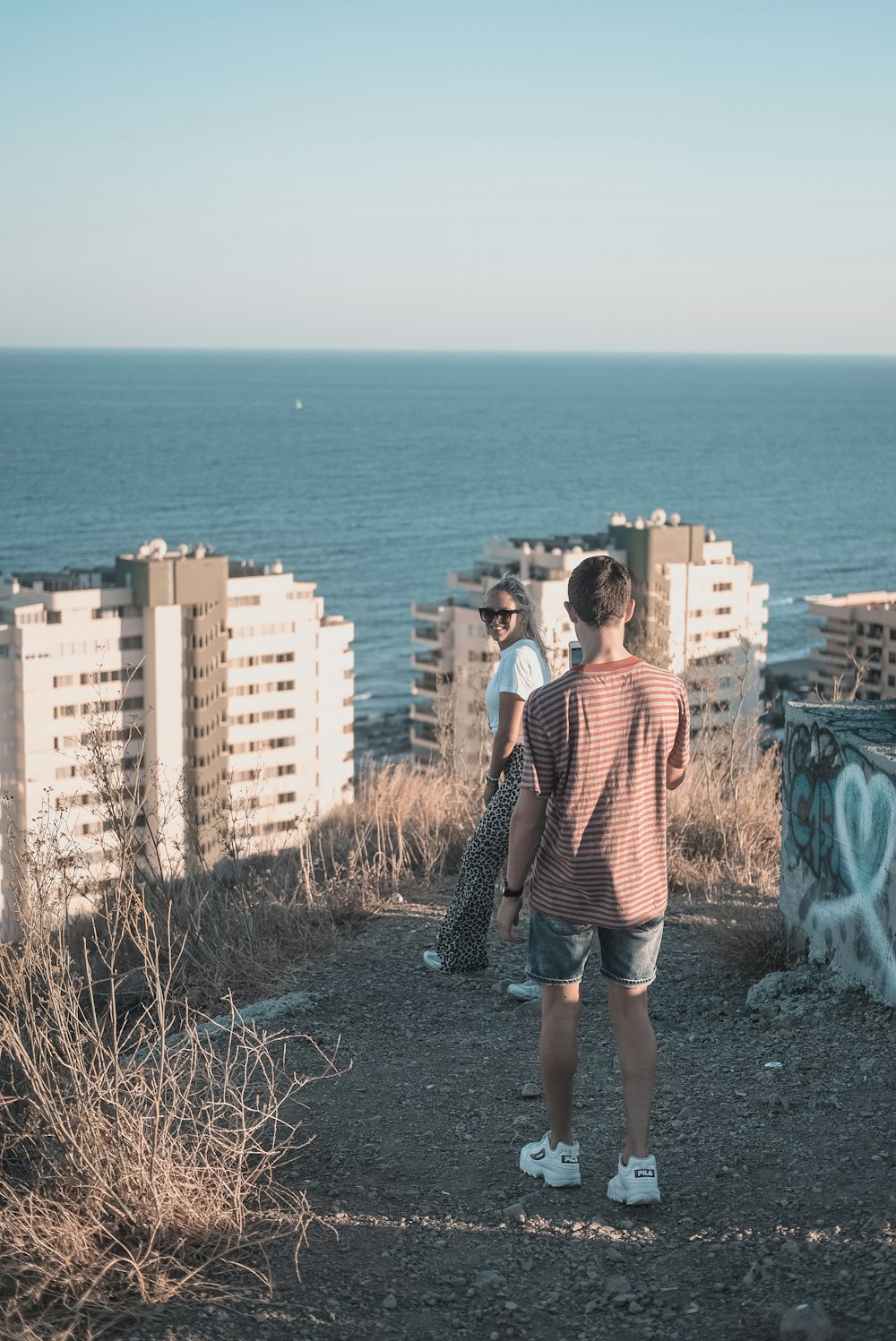 man takes photo of woman in white shirt near building overlooking sea