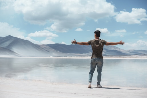 man opening his hands standing beside sea