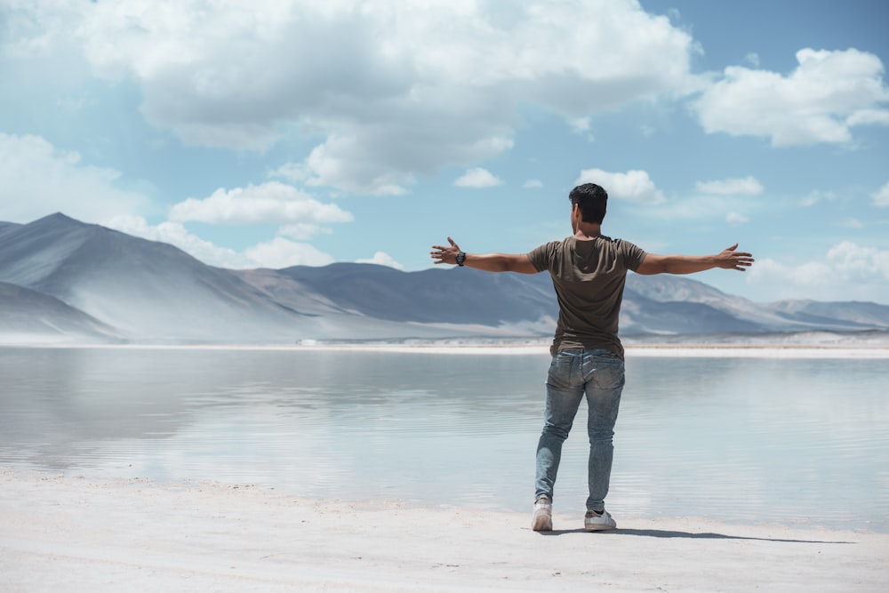 man opening his hands standing beside sea