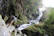 Smiling tourists hiking through lush green trails near a sparkling waterfall in San Diego, Colombia.