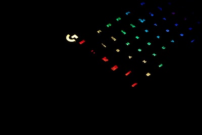 A dark setting with a partially visible gaming keyboard. The keys are illuminated with various colors including red, green, blue, and yellow, adding a vibrant contrast against the black background.