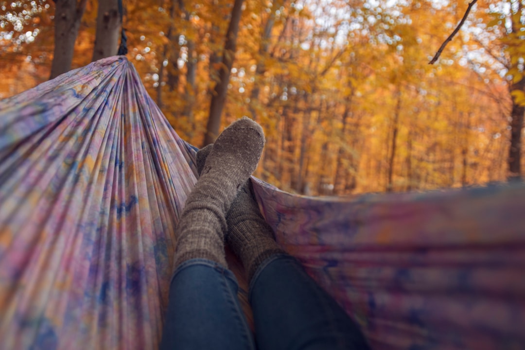 person lying wearing gray socks lying in multicolored hammock