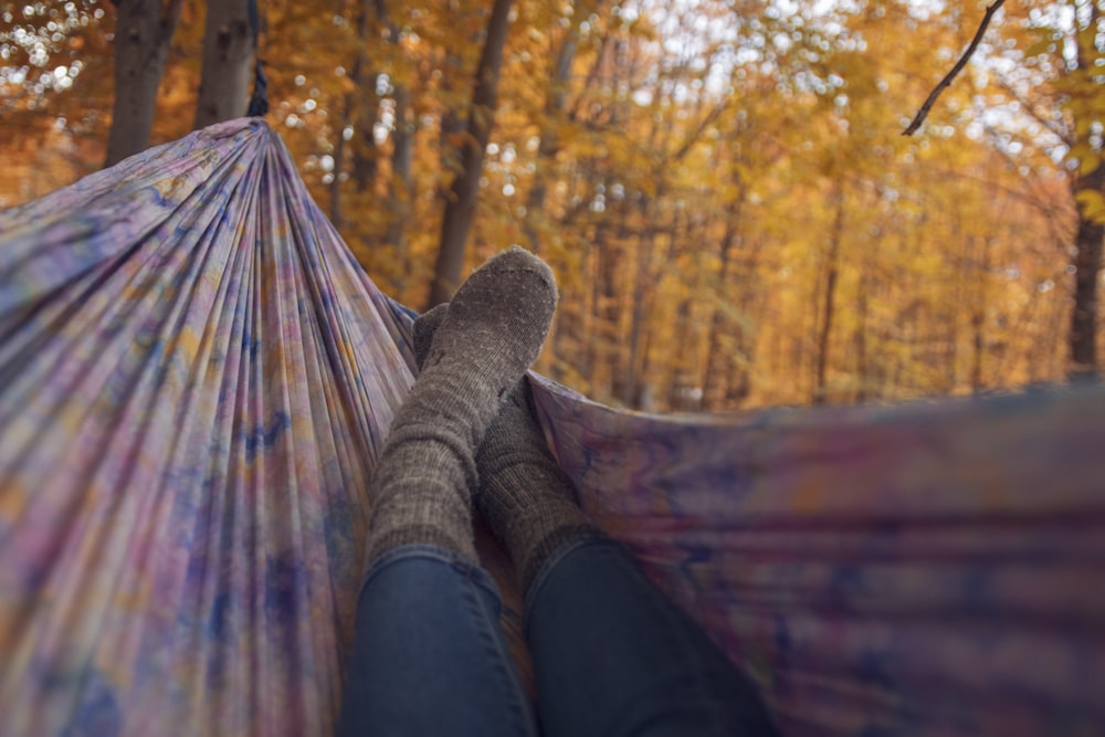 person lying wearing gray socks lying in multicolored hammock