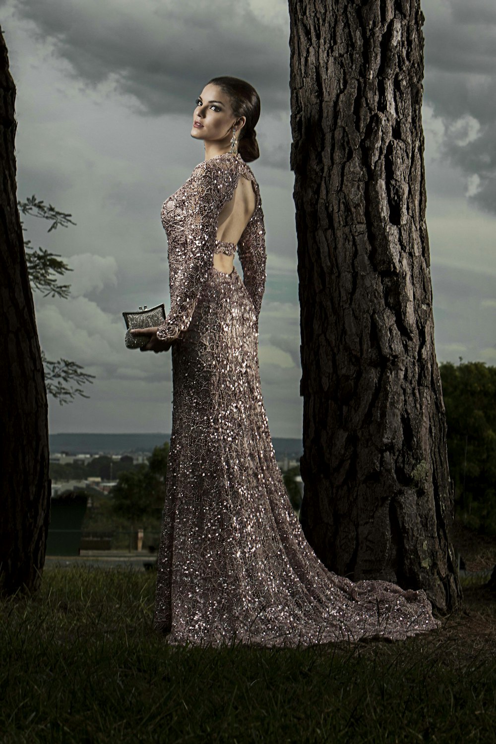 Femme en robe grise à paillettes debout à côté d’un arbre