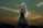 A bride in a detailed lace wedding gown holds a bouquet, veiled and illuminated dramatically against a dusky sky with golden clouds.