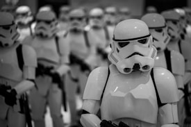 A group of identical characters wearing white futuristic armor with helmets is standing together in formation. The focus is on one character at the front, suggesting uniformity and organization.