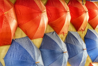 A collection of brightly colored umbrellas arranged in an overlapping pattern. The umbrellas are primarily red and blue, creating a lively and vibrant display. The texture of the fabric and the slight variations in color add depth to the image.