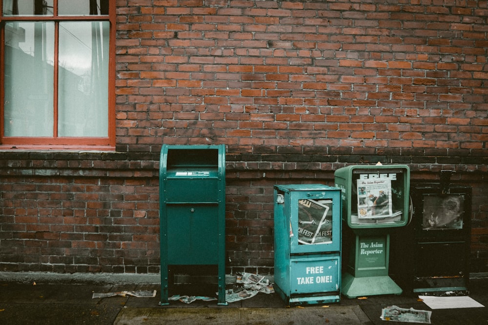 blue garbage bin beside brown bricked wall during daytime