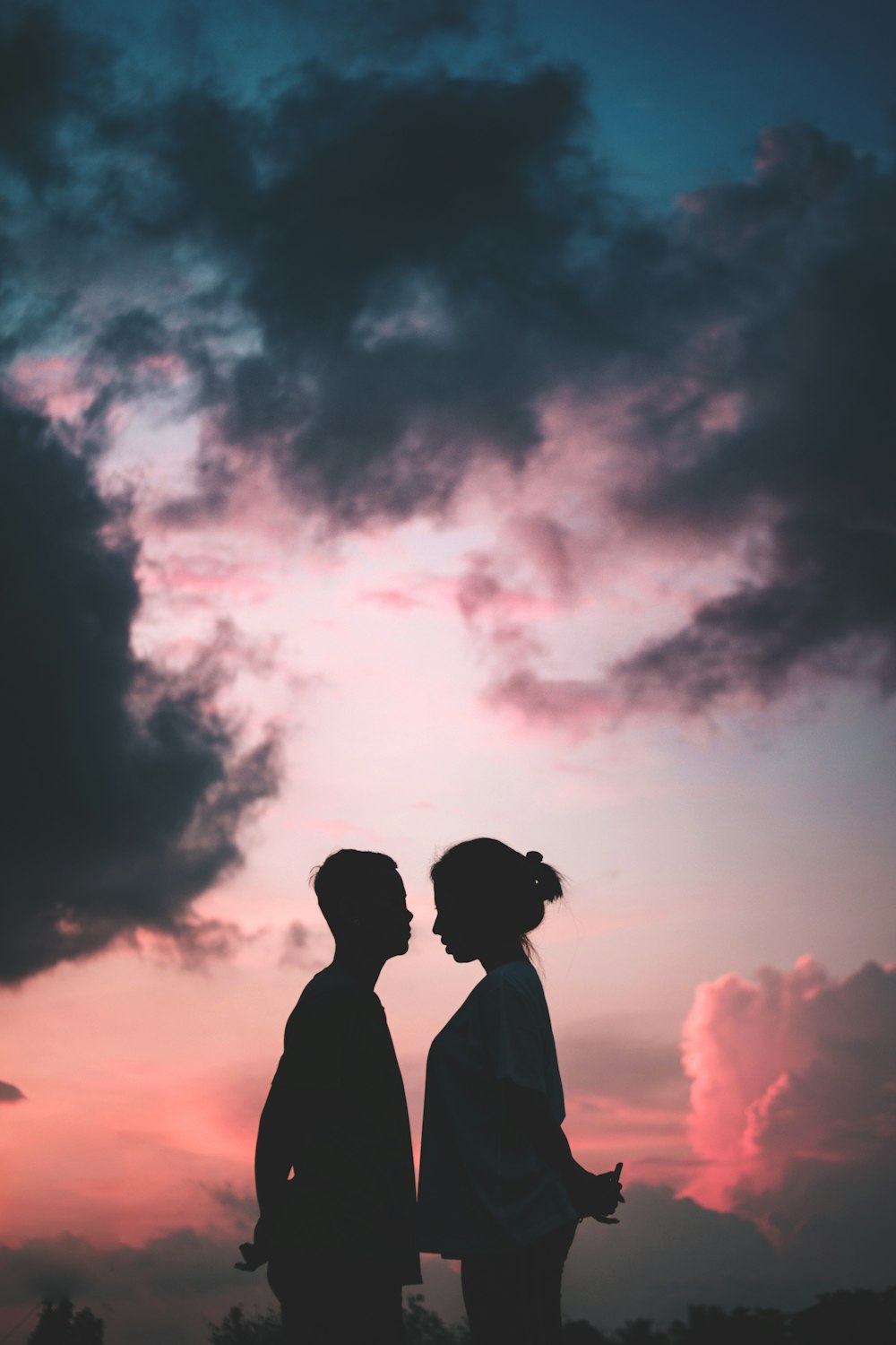 woman in white T-shirt stands in front of man under grey clouds