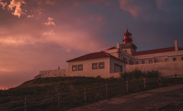 sunset view of the Crooked Lighthouse exterior with its distinctive tilted structure and surrounding greenery