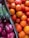 A vibrant assortment of fresh produce including bright orange oranges, deep red pomegranates, and green asparagus bundled together. The fruits and vegetables are displayed in cardboard boxes, creating a colorful and appetizing arrangement.