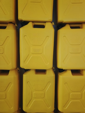 Photo of stacked jerry cans in multiple colors and sizes in a warehouse setting.