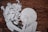 A black and white mural painted on a brick wall features a stylized depiction of a woman with voluminous hair. She is holding a round object and appears engaged in a thoughtful pose. The brick texture adds depth and character to the artwork.