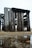 Weathered wooden pallets are stacked together in an open field. The wood appears aged and worn, with variation in texture and color. Below, there is a patch of grass and a small puddle of water reflecting part of the structure.