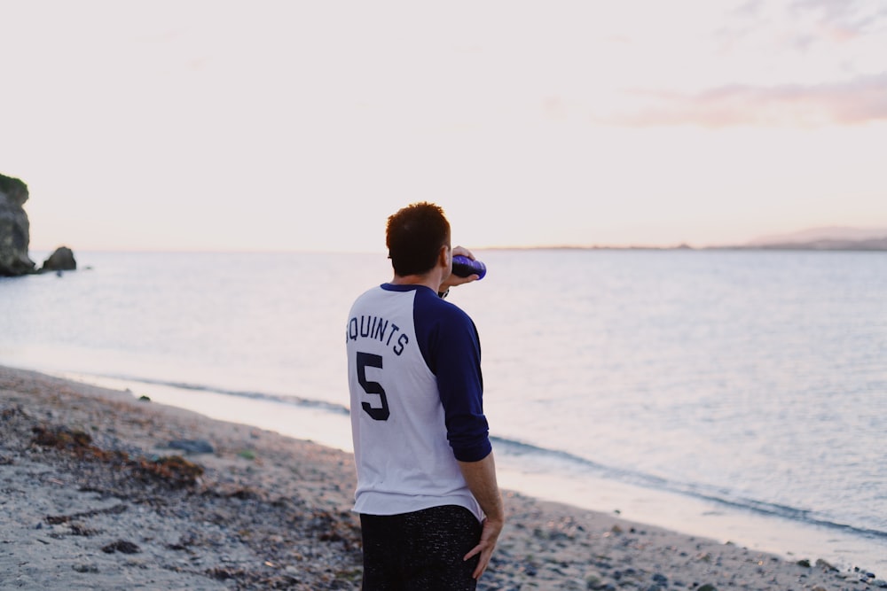 man drinking in a bottle standing in the beach