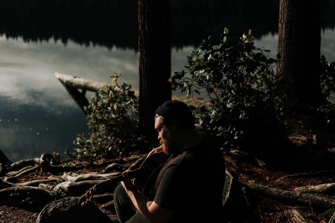 man playing guitar near trees and and body of water