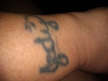 A close-up view of a tattoo on an arm featuring a simple design of a crown. The crown appears to be outlined in dark ink against the skin.