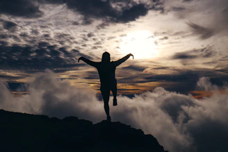 A silhouette of a person standing on a cliff edge at twilight, arms open wide embracing the horizon.
